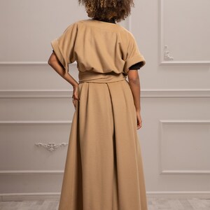 May include: A long, tan, belted coat with a wide skirt and short sleeves. The coat is made of a soft, warm fabric and has a simple, elegant design.