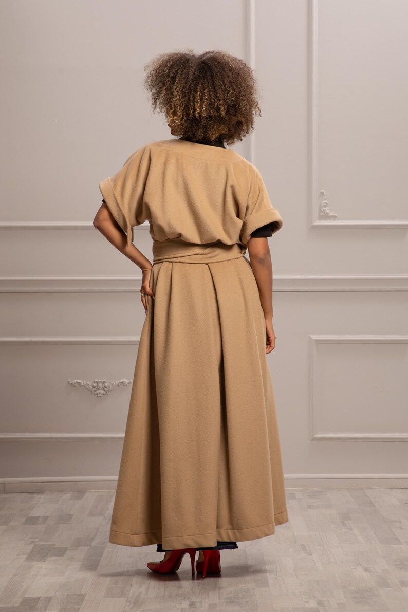 May include: A long, tan, belted coat with a wide skirt and short sleeves. The coat is made of a soft, warm fabric and has a simple, elegant design.