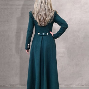May include: A long, dark green coat with a high collar and gold buttons. The coat has a fitted bodice and a flowing skirt.