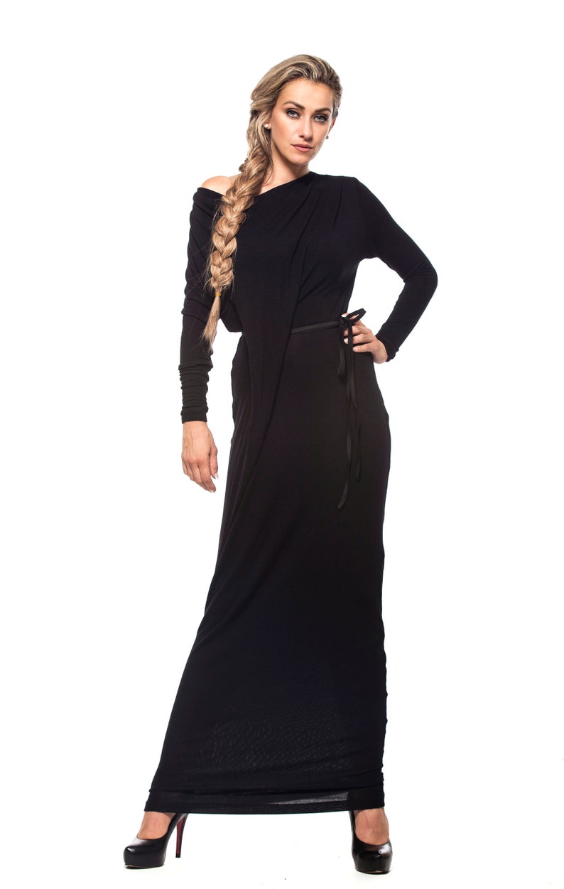 May include: A woman wearing a long black dress with a side tie. She has long blonde hair braided to the side and is wearing black heels.