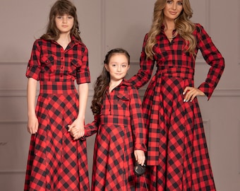 May include: Three people wearing red and black plaid dresses. The woman is holding a leash attached to a small dog wearing a matching plaid outfit.