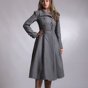 May include: A gray double-breasted coat with a flared skirt and gold buttons. The coat is worn by a person with long brown hair and is standing on a gray background.