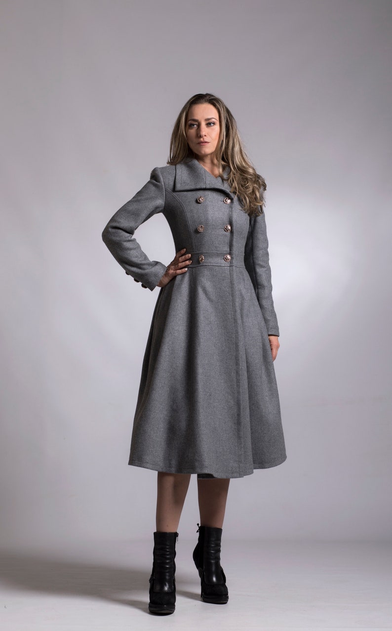 May include: A gray double-breasted coat with a flared skirt and gold buttons. The coat is worn by a person with long brown hair and is standing on a gray background.