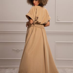 May include: A long, beige, belted coat with a wide, flowing skirt. The coat has a simple, elegant design and is made of a soft, comfortable fabric.