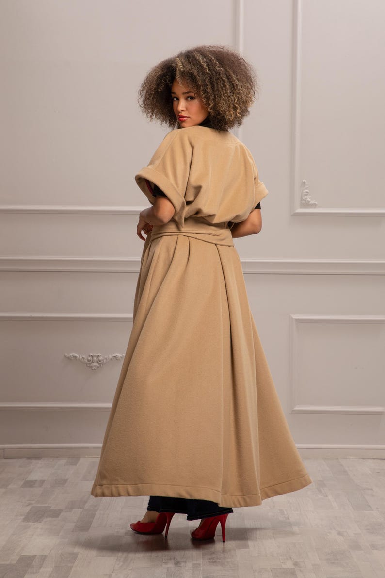 May include: A long, beige, belted coat with a wide, flowing skirt. The coat has a simple, elegant design and is made of a soft, comfortable fabric.