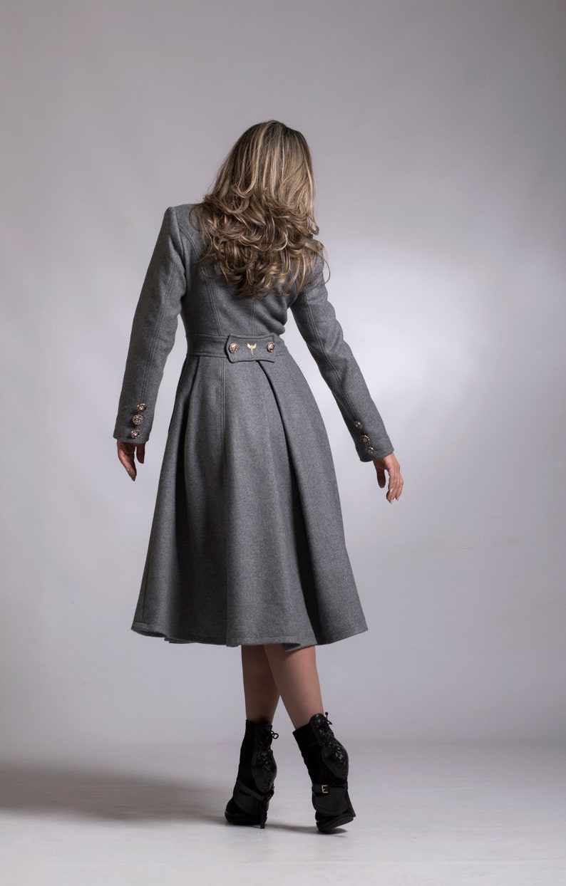 May include: A gray wool coat with a flared skirt and gold buttons. The coat has a fitted bodice and long sleeves.