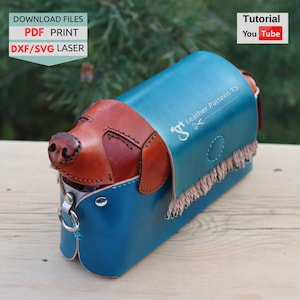 Puede incluir: Bolso de cuero artesanal con forma de perro salchicha. El bolso presenta una cabeza de perro de cuero marrón y un cuerpo azul turquesa con flecos. El texto "Leather Pattern TS" y "Download Files PDF Print DXF/SVG Laser" son visibles.