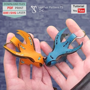 May include: Two leather keychains, one orange and one blue, are held in hands. The keychains have a bird-like design with decorative stitching. Text in the image reads "Download Files PDF Print DXF/SVG Laser" and "Leather Pattern TS".