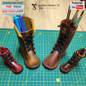 May include: Leather boot-shaped pen holders in various sizes and colors, including brown and red. The boots have black laces and are filled with pens and brushes. The image also includes text that says "DOWNLOAD FILES PDF PRINT DXF/SVG LASER" and "Tutorial You Tube".