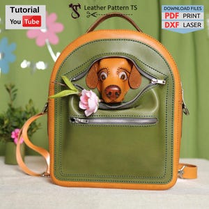 May include: A green and brown leather backpack with a dog's head peeking out of the top pocket. The backpack has a zippered pocket on the front and a flower tucked into the top pocket.