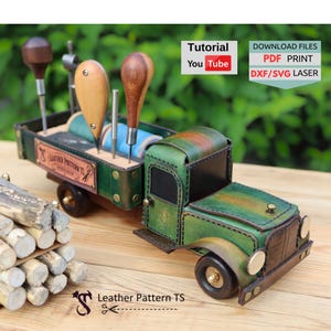 May include: A green leather truck model serving as a tool organiser, featuring wooden-handled leatherworking tools and spools of thread in the truck bed. The side displays a label reading LEATHER PATTERN TS. Text includes Tutorial YouTube and DOWNLOAD FILES PDF PRINT DXF/SVG LASER.