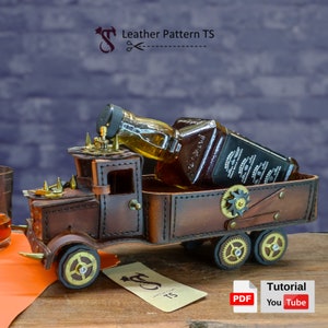Puede incluir: Un camión de cuero marrón con una botella de whisky en la caja. El camión tiene un diseño steampunk con engranajes y remaches. El camión está sobre una superficie de madera con un paño naranja en primer plano. La imagen incluye el texto "Leather Pattern TS" y "Tutorial".