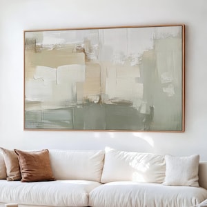 May include: A large rectangular abstract painting featuring layered brushstrokes in shades of sage green, cream, beige, and white, enclosed in a thin wooden frame and displayed on a white wall above a white sofa with brown and white throw pillows.