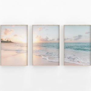 May include: A set of three framed prints featuring a beach scene with a soft, pink and blue sky, turquoise water, and white foamy waves crashing on the shore.