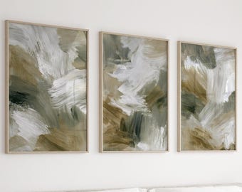 Peut inclure: Un ensemble de trois impressions d'art mural rectangulaires présentant des coups de pinceau abstraits dans des tons de blanc, beige, vert olive et gris foncé. Chaque impression est encadrée d'un fin cadre en bois clair.