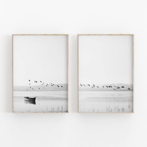 Op de afbeelding: Een zwart-witfoto van een klein bootje op een rustig meer met een zwerm vogels die erboven vliegen. De afbeelding is in twee frames gesplitst.