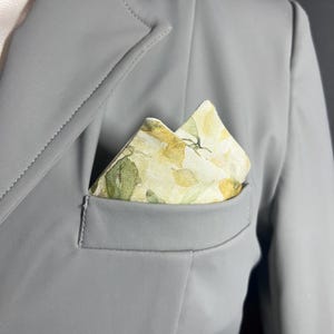 May include: A gray jacket with a floral patterned pocket square. The pocket square has a white background with yellow and green flowers.