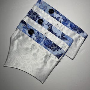 Könnte beinhalten: Drei weiße Satin-Gesichtsmasken mit blauen und weißen Blumenmustern. Jede Maske hat einen Knopfverschluss.