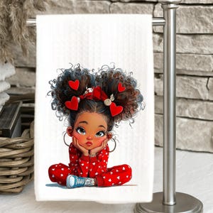 May include: White hand towel featuring a cartoon illustration of a girl with dark curly hair adorned with red heart accents. The girl is wearing a red onesie with white hearts and blue sneakers. The towel is hanging on a silver towel rack.