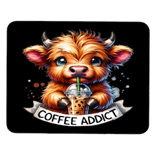 May include: A cartoon illustration of a brown and white Highland cow with big blue eyes drinking a coffee beverage from a clear cup with a green straw. The text "COFFEE ADDICT" is written in white on a banner behind the cow.