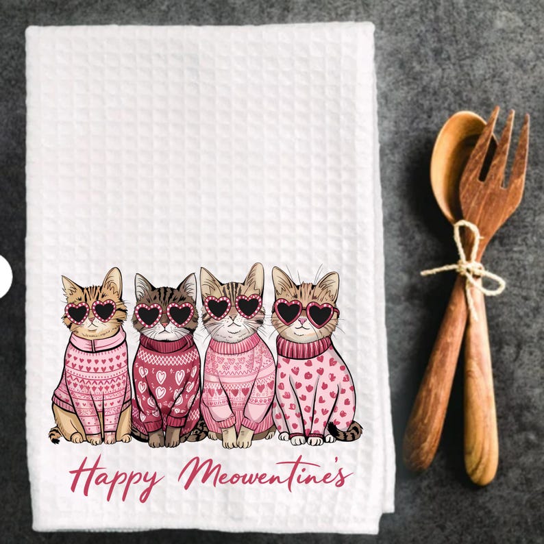 Peut inclure: Serviette de cuisine blanche avec un motif rose et blanc de quatre chats portant des lunettes en forme de c&oelig;ur et des pulls roses. Le texte "Happy Meowentines" est imprim&eacute; sous les chats.