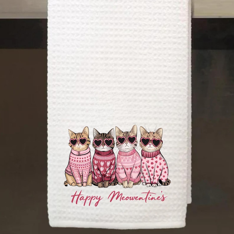 Peut inclure: Serviette de cuisine blanche avec quatre chats portant des pulls roses et des lunettes de soleil en forme de c&oelig;ur. Le texte "Happy Meowntimes" est imprim&eacute; sous les chats.