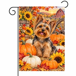 Puede incluir: Una bandera de jardín rectangular que muestra un Yorkshire Terrier con un lazo de cuadros naranja, rodeado de calabazas naranjas y blancas, girasoles amarillos brillantes y hojas de arce otoñales, con un granero rojo al fondo.