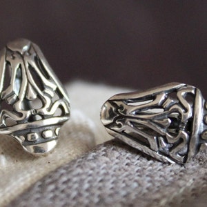 May include: Two silver-colored, ornate earrings with a detailed, openwork design. The earrings have a teardrop shape with a decorative base. The intricate patterns and polished finish suggest a vintage or handcrafted style.