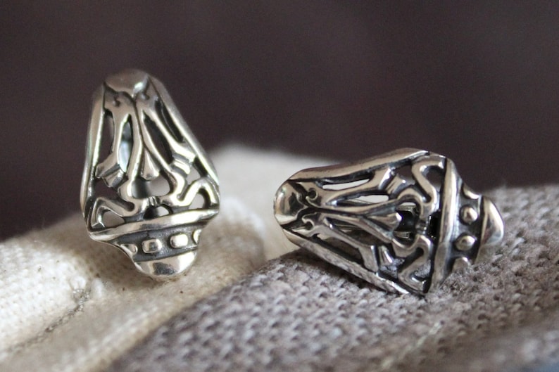 May include: Two silver-colored, ornate earrings with a detailed, openwork design. The earrings have a teardrop shape with a decorative base. The intricate patterns and polished finish suggest a vintage or handcrafted style.