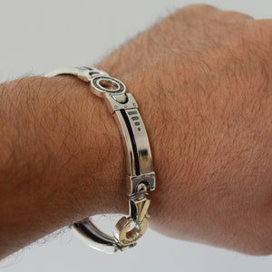 May include: A silver bracelet with a unique design is shown. The bracelet features a series of rectangular and circular links, with a contrasting black inlay. The clasp is gold-toned. The bracelet is approximately 8 inches (20 cm) in circumference.