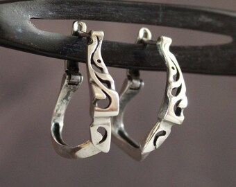May include: A pair of silver hoop earrings with a delicate, intricate design. The earrings are made of a smooth, polished metal and have a slightly curved shape.