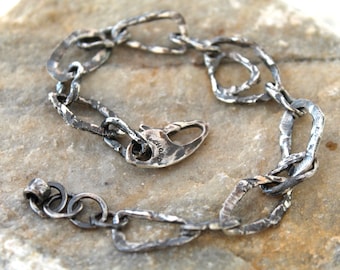 May include: A dark silver-toned chain bracelet featuring irregular, textured, hand-hammered links. The bracelet includes a lobster claw clasp and a small circular end ring, showcasing a weathered, oxidized finish across all metal components.