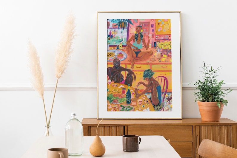 May include: A colorful painting of three people sitting around a table with food and drinks. The painting is set in a kitchen with a pink wall and yellow cabinets. The people are all wearing casual clothing and have dark skin. The painting is framed in gold.