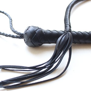 May include: A black leather bullwhip with a braided handle and a long tassel. The whip is made of high-quality leather and is designed for use in equestrian sports or as a prop.