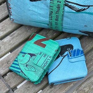 May include: Two wallets made from recycled plastic bags. The wallets are blue and green with a fish design. The text on the green wallet reads "LƯỢN on on".