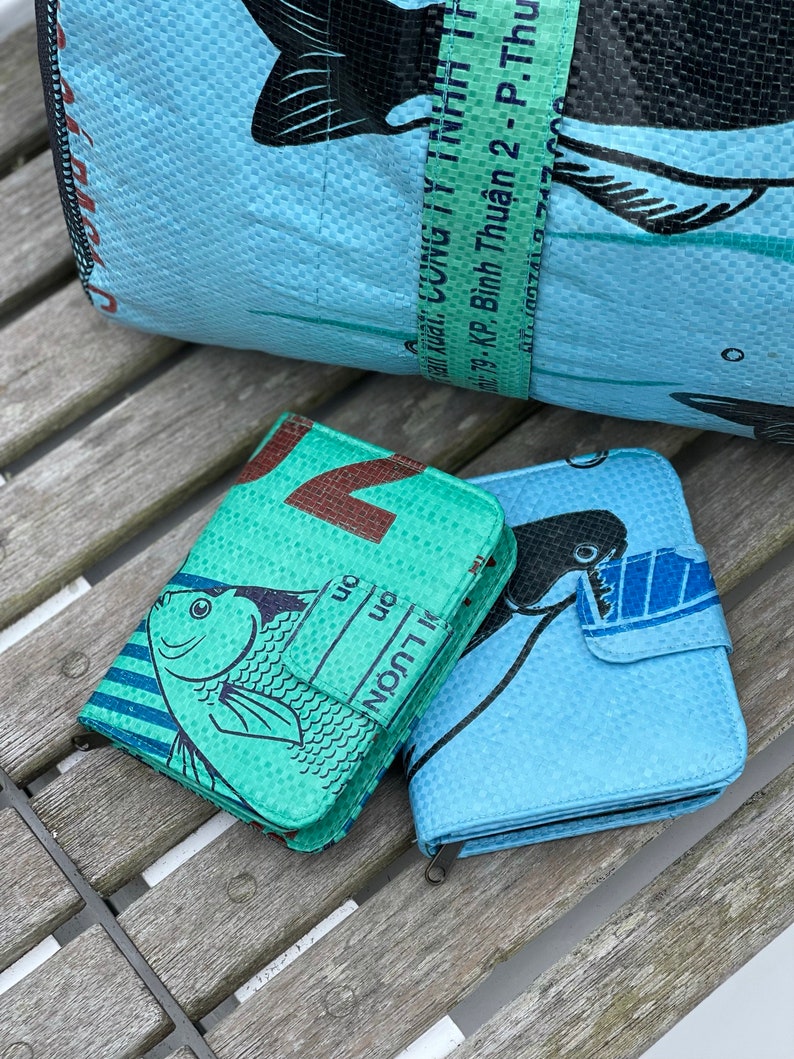 May include: Two wallets made from recycled plastic bags. The wallets are blue and green with a fish design. The text on the green wallet reads "LƯỢN on on".