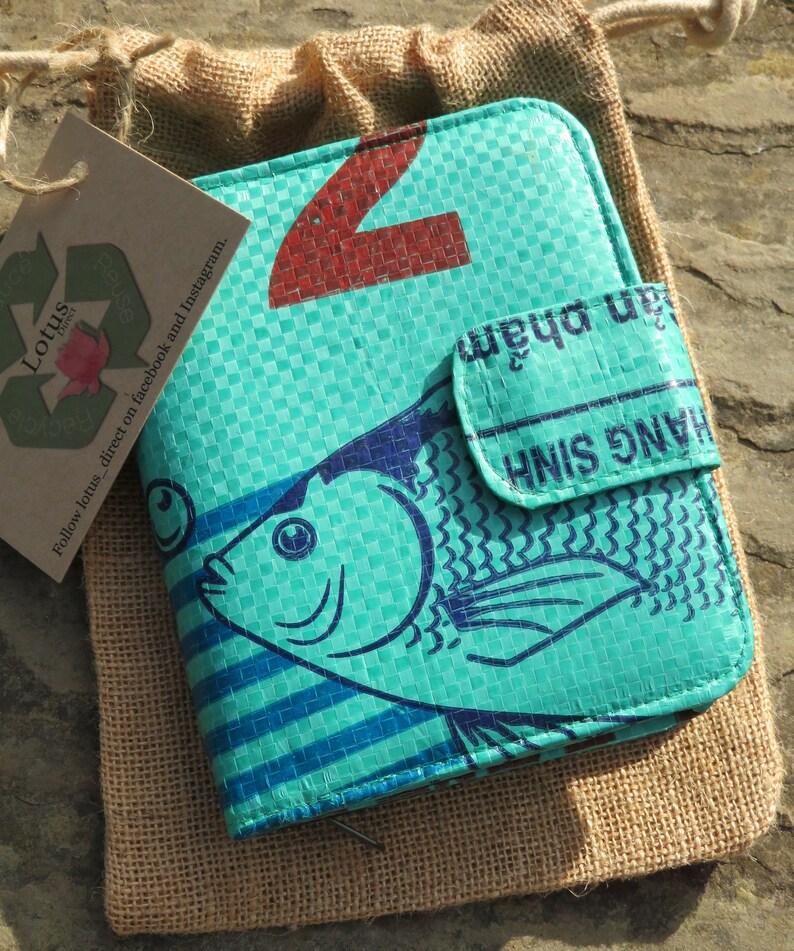 May include: A turquoise blue wallet with a fish design and the text "H&Agrave;NG SINH" and "jan phẩm" printed on it. The wallet is made from recycled materials and has a zipper closure.