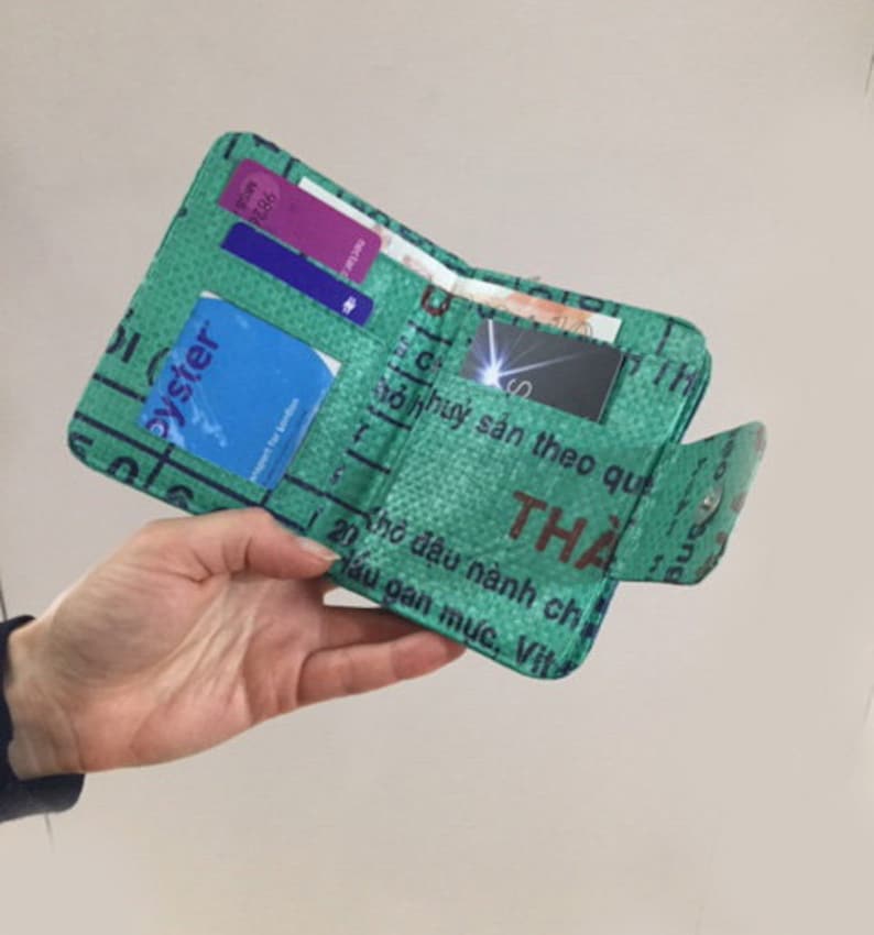 May include: A green wallet made from recycled materials. The wallet is folded closed and has several cards inside. The wallet has text in Vietnamese on the outside.