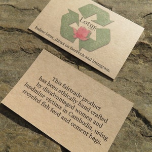 May include: A brown paper business card with a green recycling symbol and the text "Lotus Direct" and "Follow lotus_direct on facebook and Instagram." The card also includes the text "This fairtrade product has been ethically hand crafted by disadvantaged women and landmine victims in Cambodia, using recycled fish feed and cement bags."