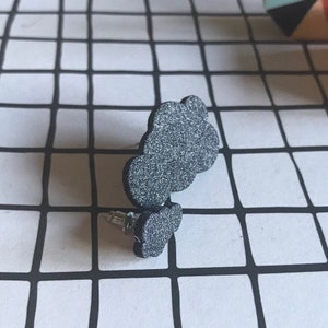 May include: A pair of black glitter cloud-shaped earrings. The earrings are made of a lightweight material and have a post back.