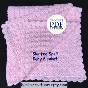 May include: A pink crocheted baby blanket with a slanted shell stitch pattern. The blanket is folded in half and has a scalloped edge. The text "CROCHET PDF PATTERN" and "Slanted Shell Baby Blanket" is visible on the blanket. The website address "Haniascreations.etsy.com" is also visible.