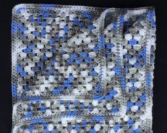 May include: A handmade crochet blanket in a granny square pattern. The blanket features a color scheme of white, gray, and blue. The edges are neatly finished with a blue border, creating a cozy and inviting aesthetic. This blanket is perfect for a baby.