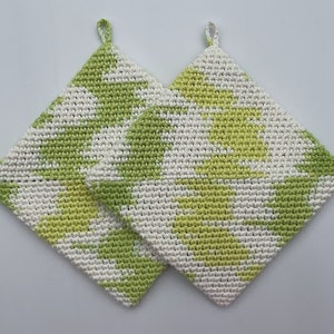 May include: Two crocheted pot holders in a green and white geometric pattern. The pot holders are square shaped and have a loop at the top for hanging.