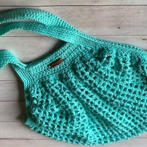 May include: A turquoise crocheted tote bag with a single, double-layered strap. The bag is made with a simple, open stitch pattern.