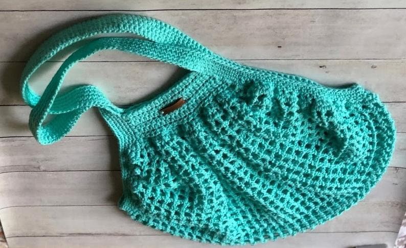 May include: A turquoise crocheted tote bag with a single, double-layered strap. The bag is made with a simple, open stitch pattern.