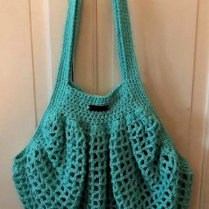 May include: A turquoise crocheted tote bag with a black handle. The bag has a mesh design and is hanging on a white door.