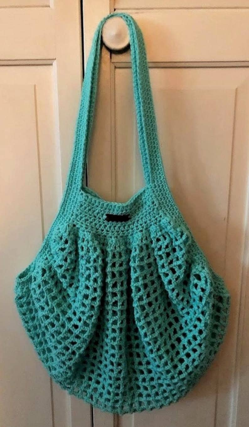 May include: A turquoise crocheted tote bag with a black handle. The bag has a mesh design and is hanging on a white door.