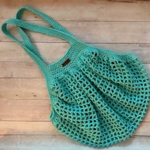 May include: A turquoise crocheted tote bag with a brown leather tag. The bag has a wide, open top and a mesh design.