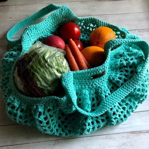 May include: A teal blue crocheted mesh bag filled with produce, including a head of lettuce, carrots, oranges, and tomatoes.