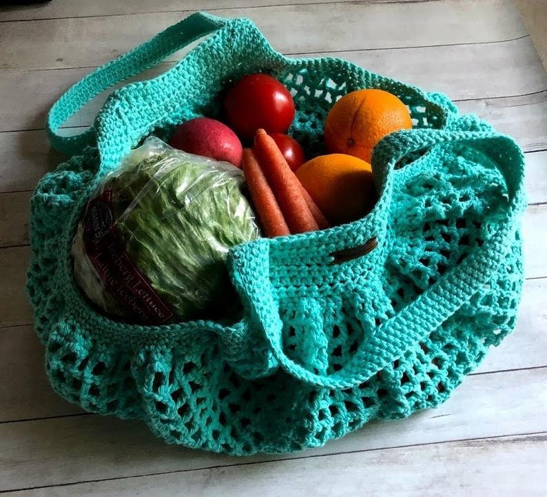 May include: A teal blue crocheted mesh bag filled with produce, including a head of lettuce, carrots, oranges, and tomatoes.